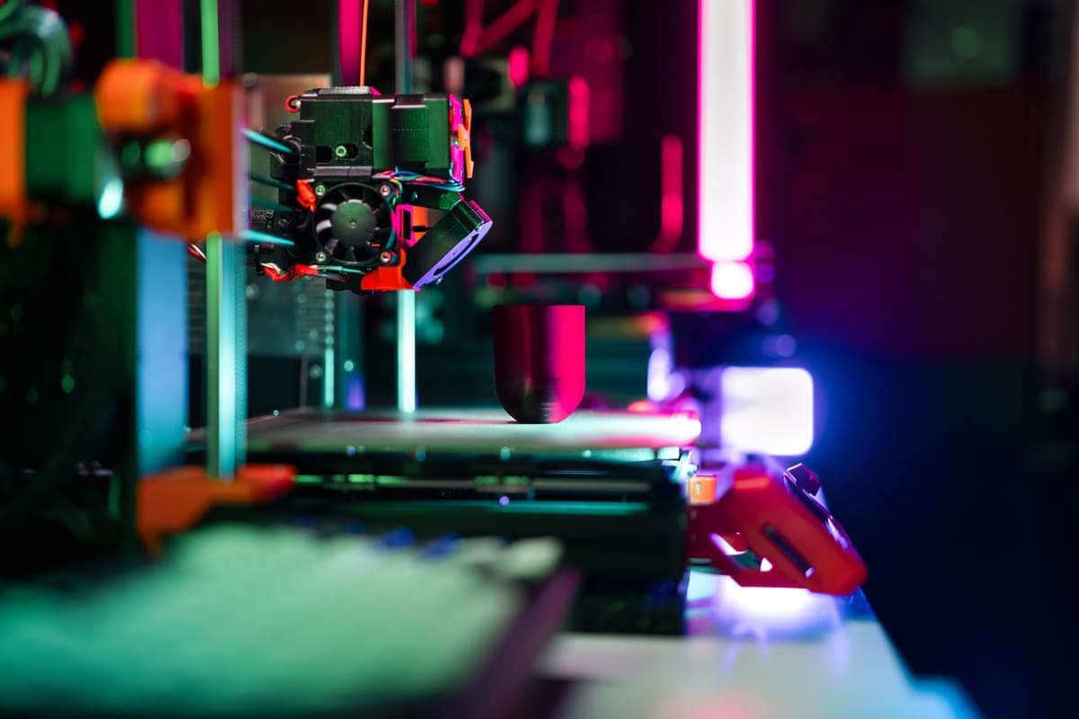 A full-size open-frame 3D printer with a large build plate, lit from one side