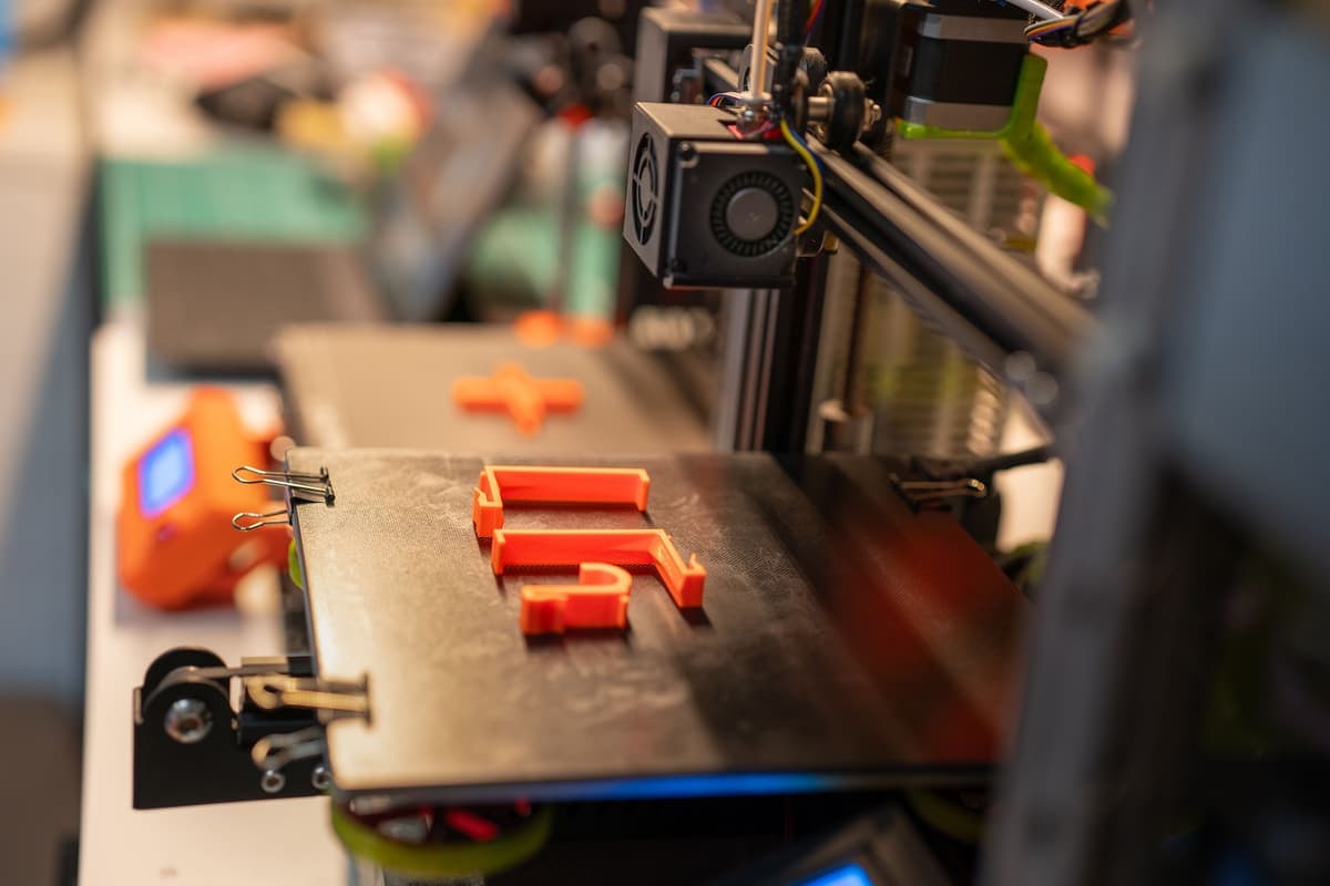 A 3D printer building an orange plastic part