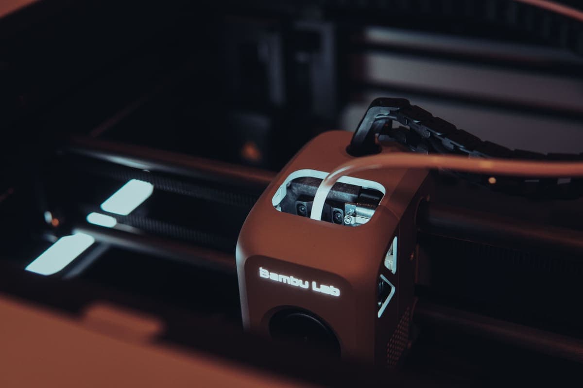 The toolhead of a Bambu Lab 3D printer mid-print, lit against a dark background