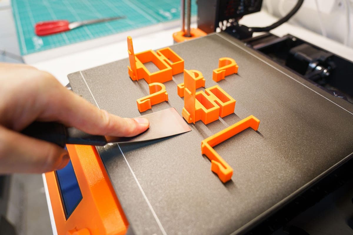 A hand reaching over a 3D printer partway through a print