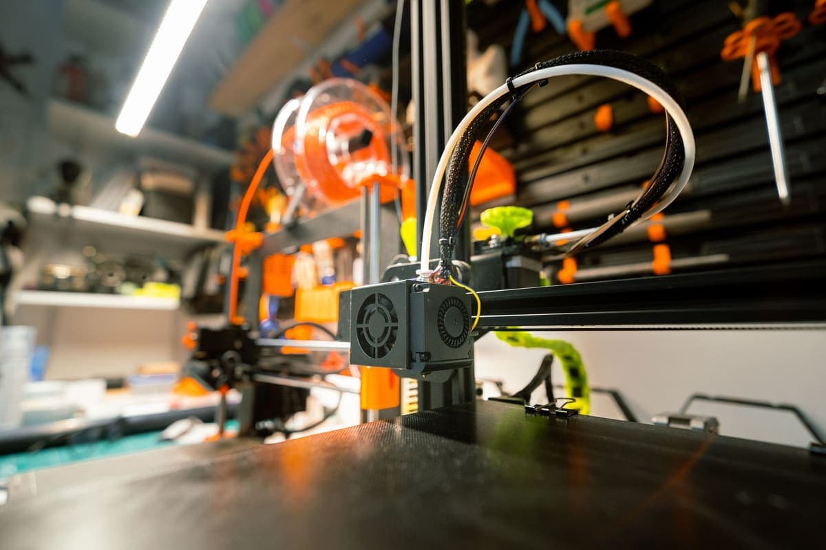 A desktop 3D printer in a workshop with a filament spool and hand tools