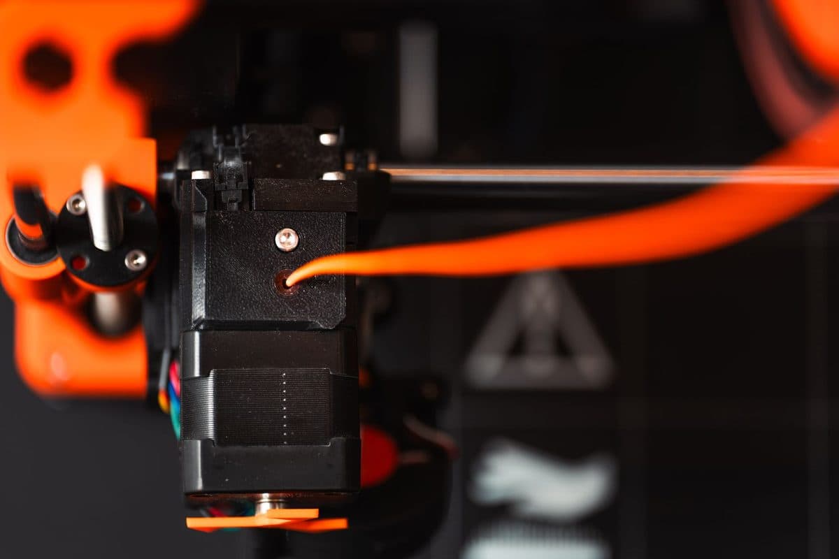 A 3D printer extruder feeding orange filament