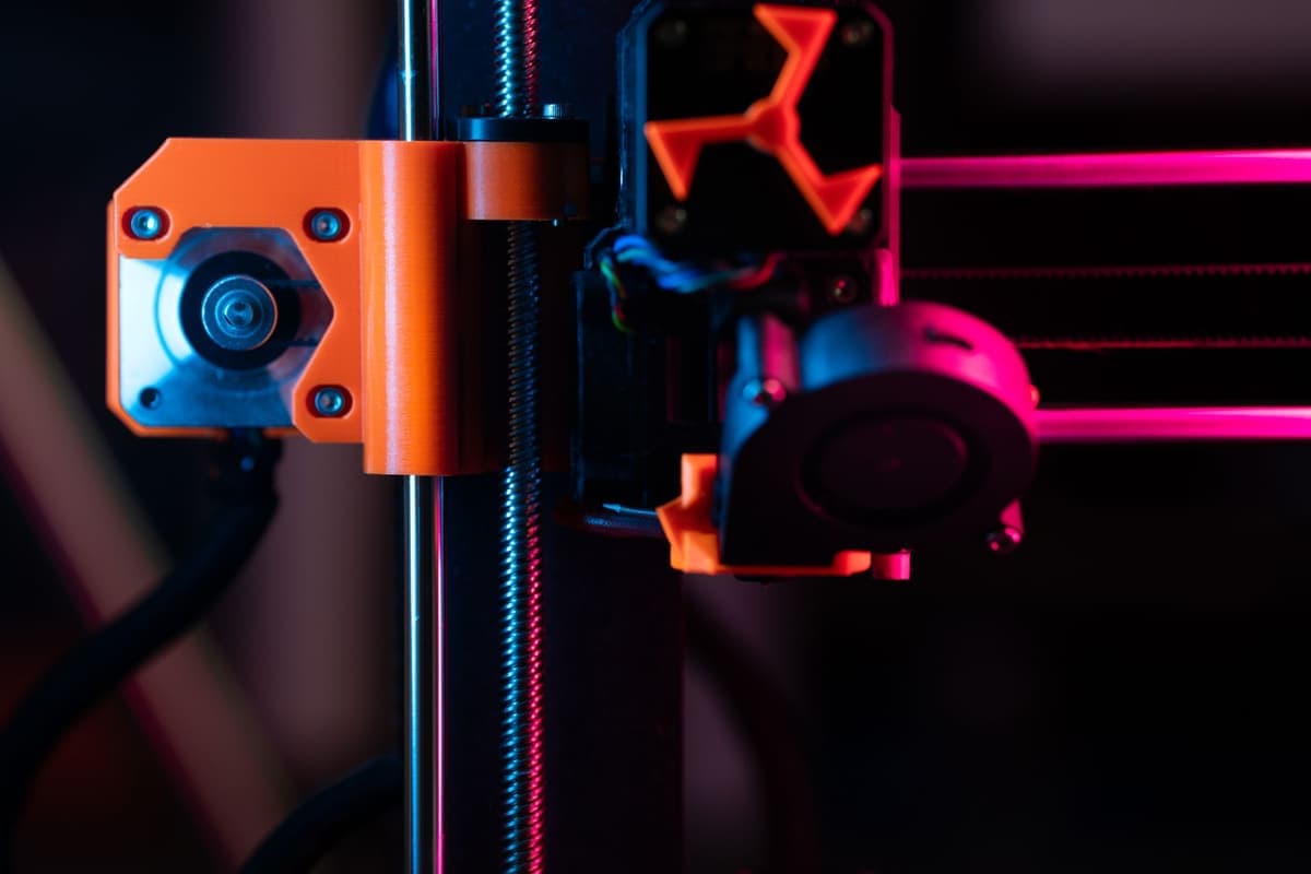 A close-up of a 3D printer's extruder and nozzle assembly lit from the side