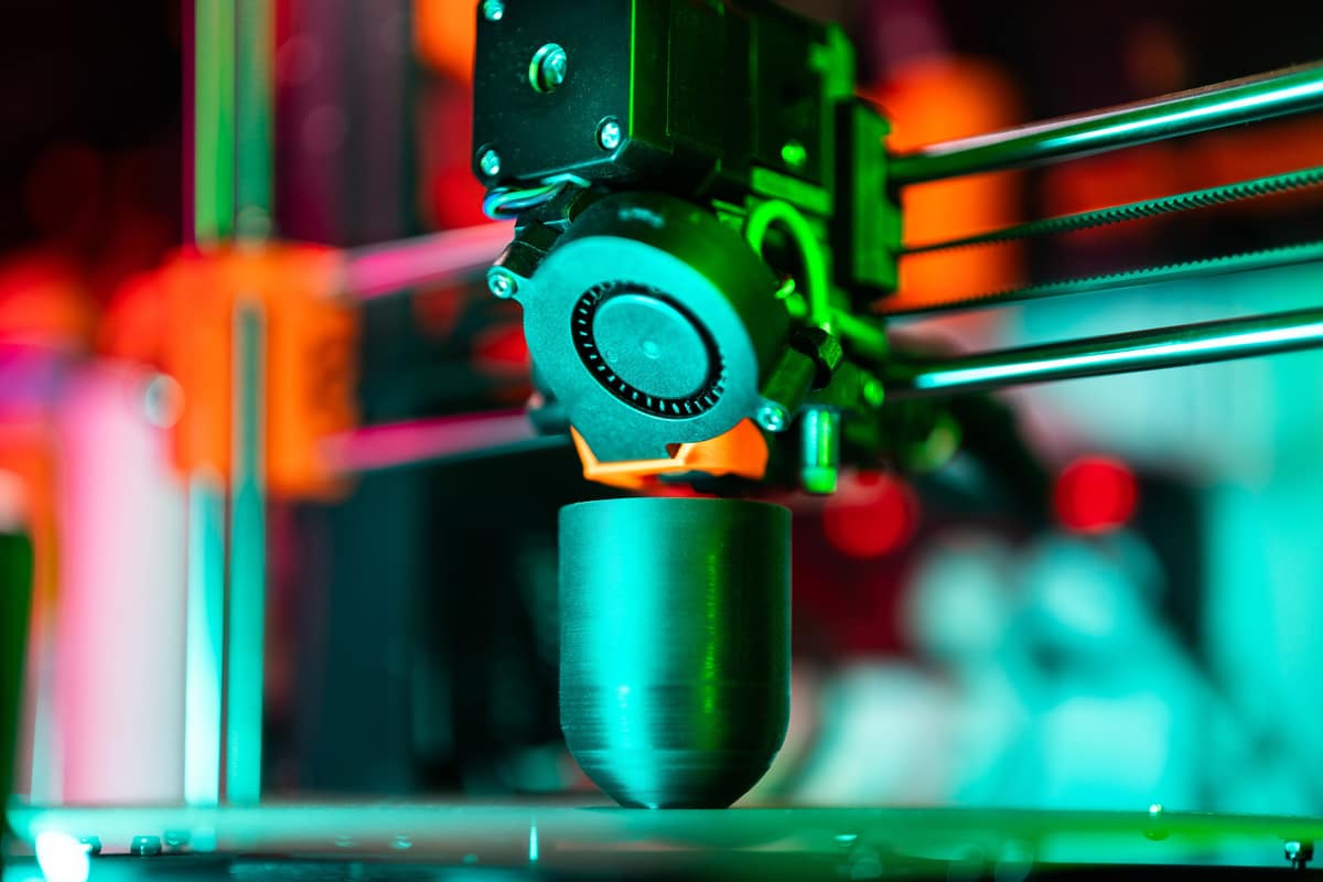 A 3D printer building a part under colored light