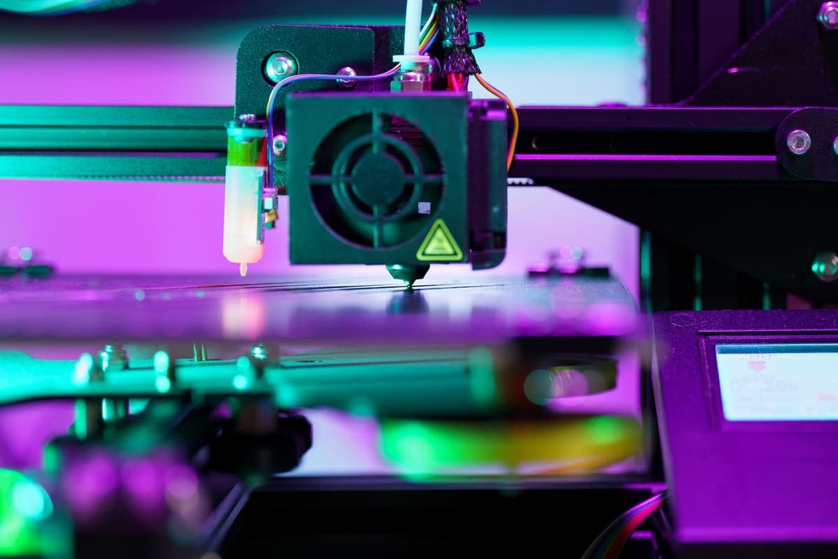 The print head of a 3D printer photographed close up under colored light