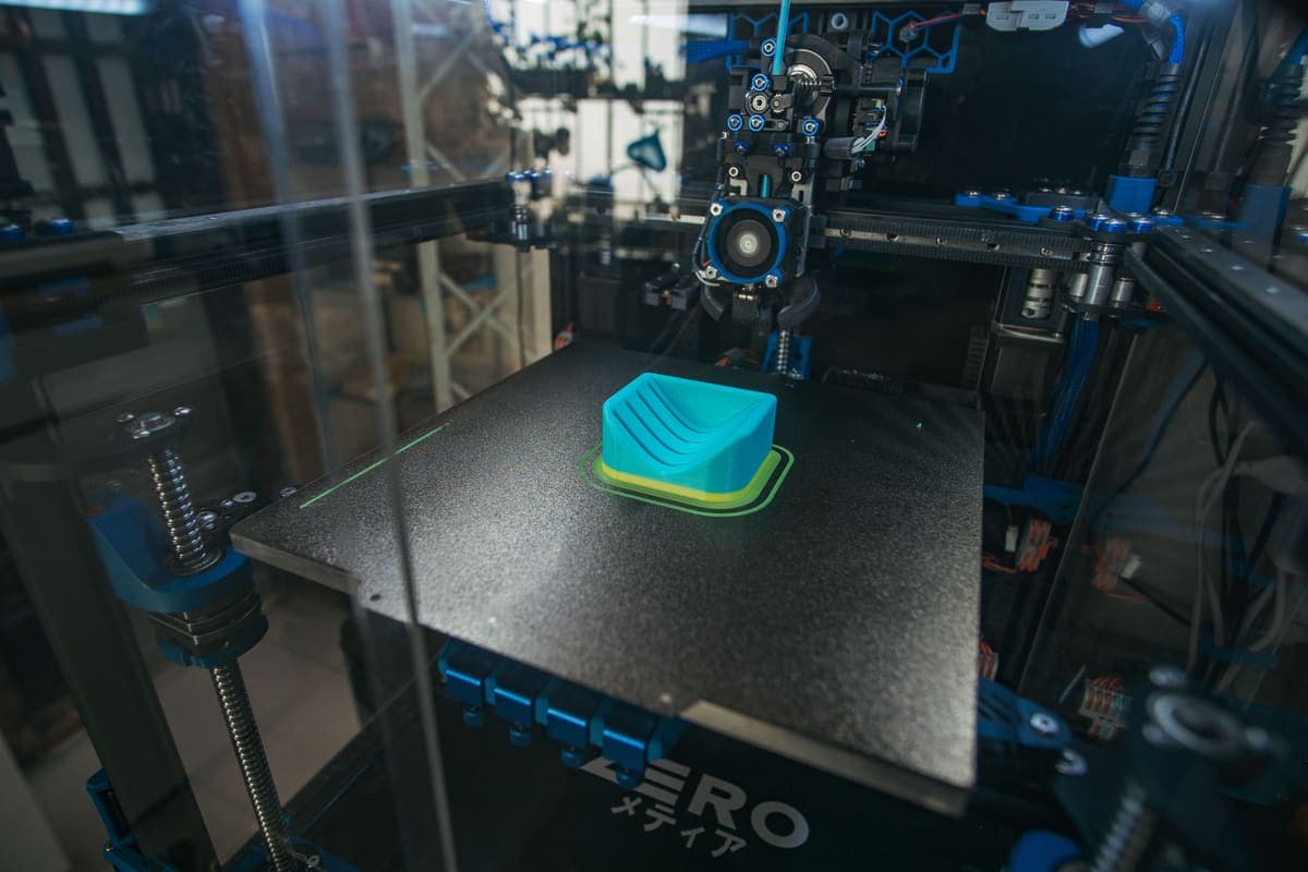 An enclosed desktop 3D printer building a plastic object, seen through the front panel