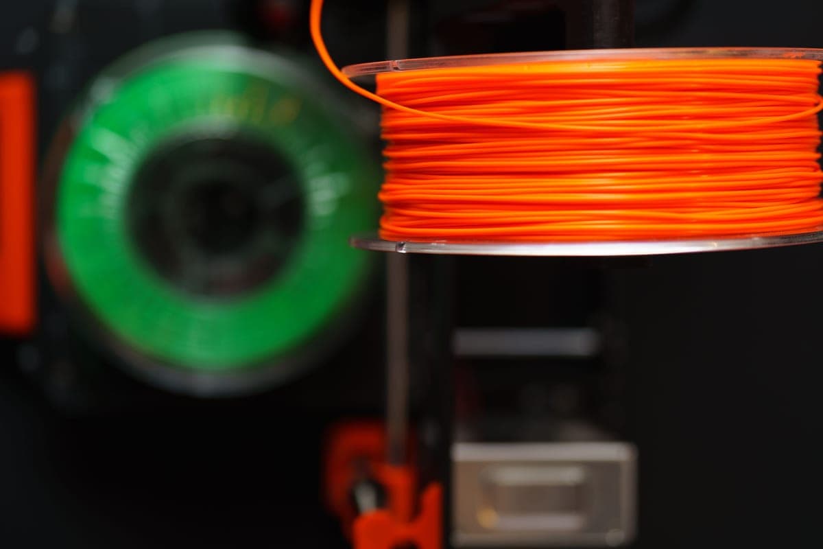 Two spools of filament side by side, one PLA and one PETG, on a dark workbench