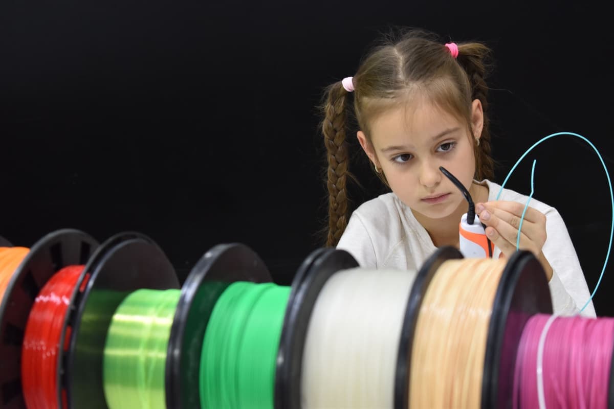 Spools of colored 3D printer filament beside a printer