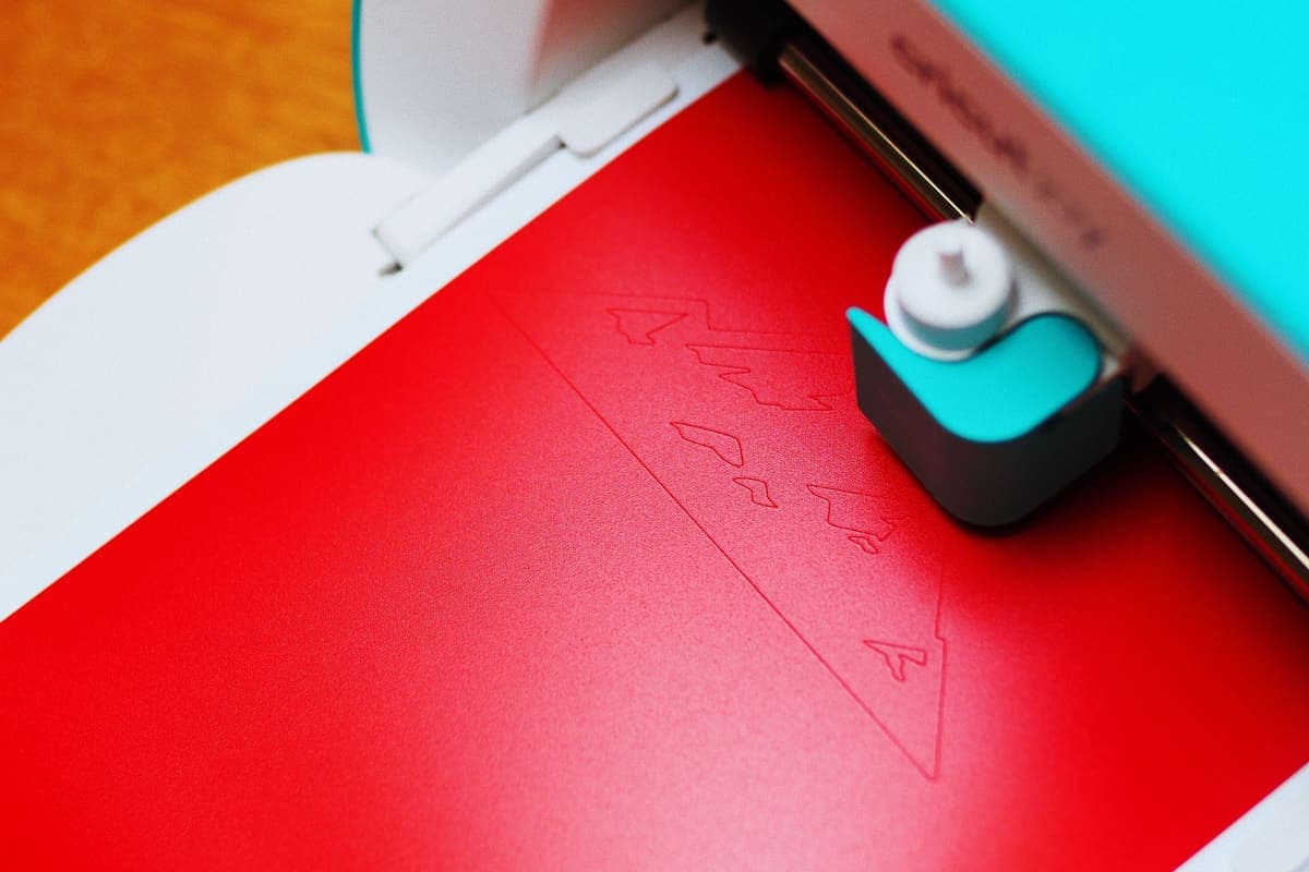 A craft cutting machine working through a sheet of red paper
