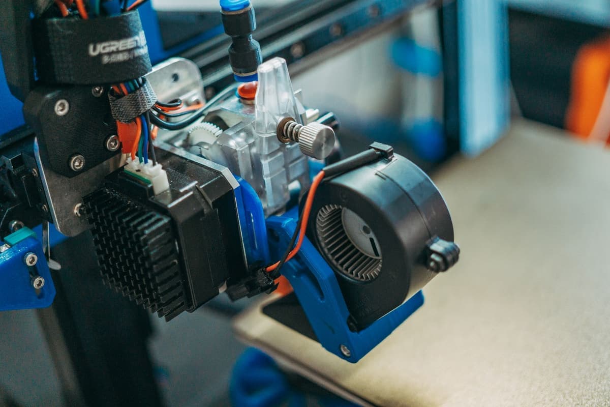 A close-up of 3D printer internals showing wiring and mechanical parts in a workshop