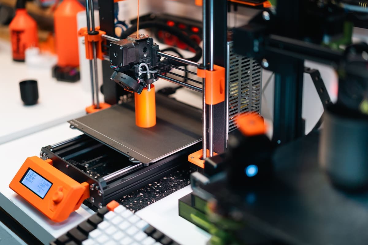 A 3D printer working in a workshop, building an orange prototype